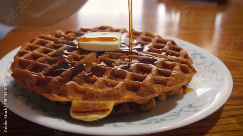 Pouring maple syrup onto a golden brown waffle at brunch in 4k. A pat of butter melts into the stack of waffles. Vermont maple syrup pours from a ceramic crock. The breakfast food is a family favorite