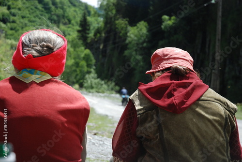 Dwie staruszki siedzą na ławce  i patrzą na chłopca jadącego na rowerze