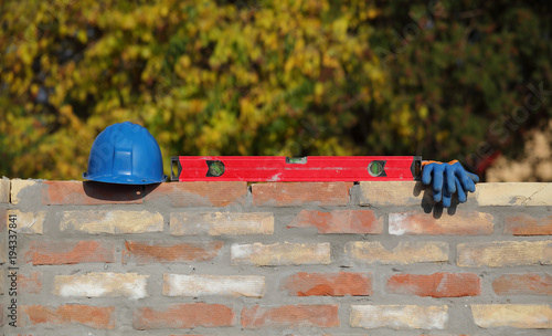 Mason tool and equipment at brick wall, level tool, gloves and helmet, construction site photo