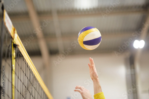 The volleyball player's hand in the covered gym fights the ball in front of the net,