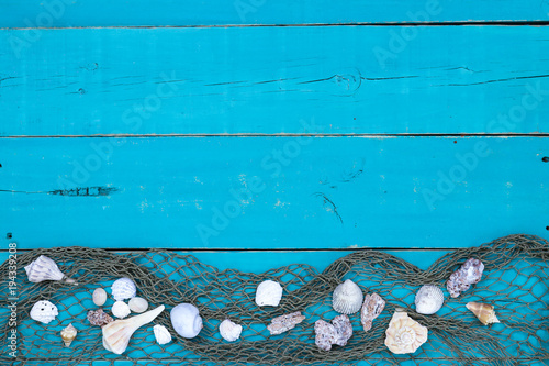 Blank rustic antique teal blue wood sign with seashells and fish netting border; wooden background with copy space
