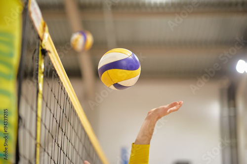 The volleyball player's hand in the covered gym fights the ball in front of the net, photo