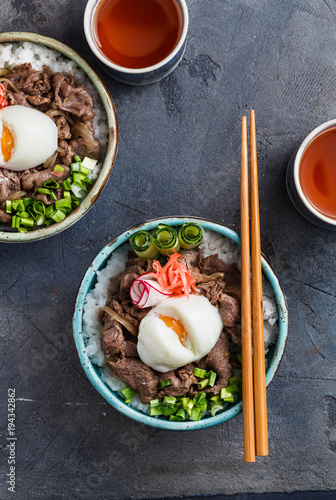 Close view of beef and rice bowl topped with egg and onion