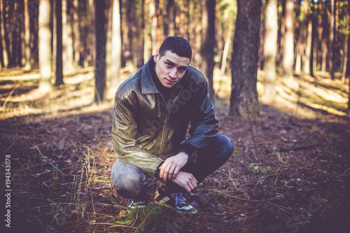 A young man of criminal appearance in a black leather jacket posing in an autumn forest. photo