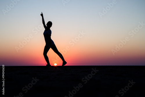 A silhouette of a girl dancing front of a sunset
