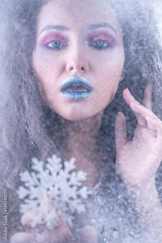 Fototapeta Naklejka Na Ścianę i Meble -  Young attractive girl in bright art-makeup, with snowflake behind the glass