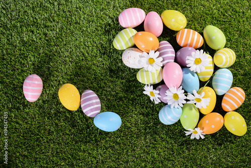 above top view of multi colored painted easter eggs on green grass with springtime daisy flowers