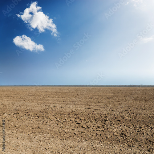 black plowed agriculture field and blue sky with clouds