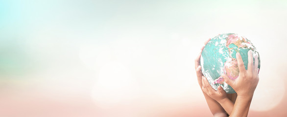 Earth Day concept with many hands holding globe together for world unity and environmental protection on nature background with bokeh and copy space for global conservation