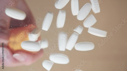 White prescription pills fall directly onto the lens in slow motion. The pain killer tablets represent pharmaceutical substance abuse in teens and recreational drug use of opiates.