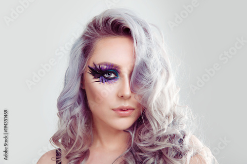 Beautiful woman with artistic purple blue eyes makeup feather on eyelashes and curly hair