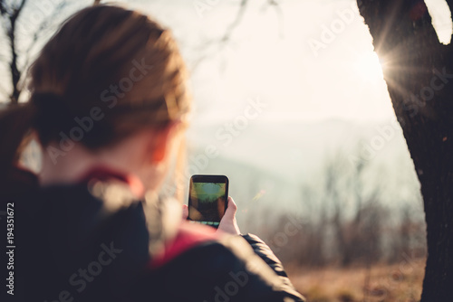 Girl taking photos with smart phone in forest