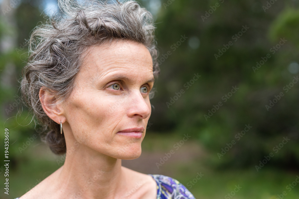 Profile of middle aged woman with grey hair against forest background (selective focus)