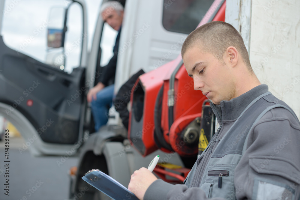 Man writing on clipboard while lorry driver waits