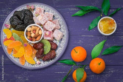 Set of eastern desserts. Marmalade  kivi  prunes  rahat lokum  nuts  mandarin  persimmon  dried apricots  pistachios  dates  raisins in a colorful blue plate. Wooden rustic background. Top view