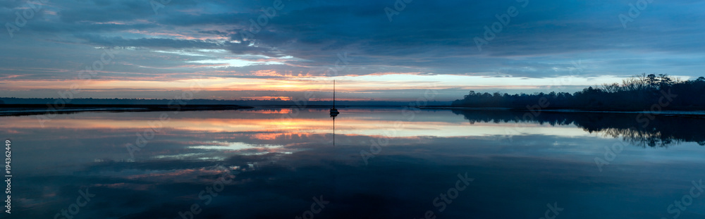 A calm morning at sunrise with a sailboat ready to depart for the day.