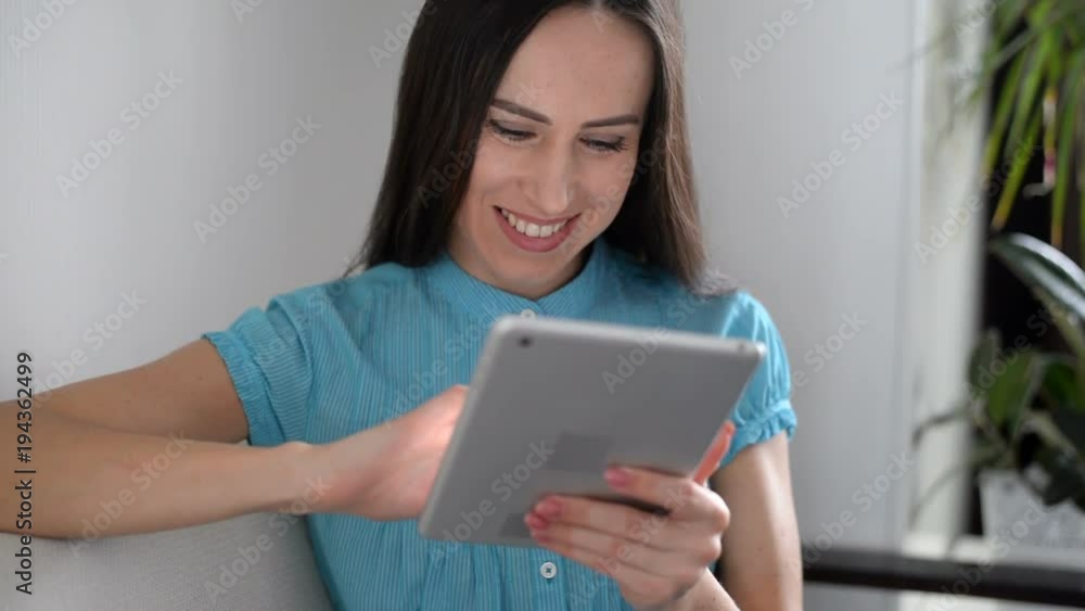 Pleased girl using tablet computer touchscreen while sitting on the sofa Pleased girl using tablet computer touchscreen while sitting on the sofa