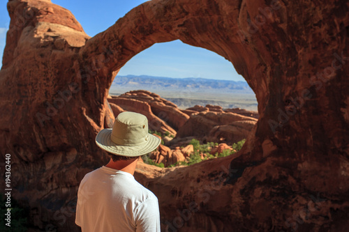 Fototapeta A hiker looking back through the Double-O Arch in Arches National Park, Utah