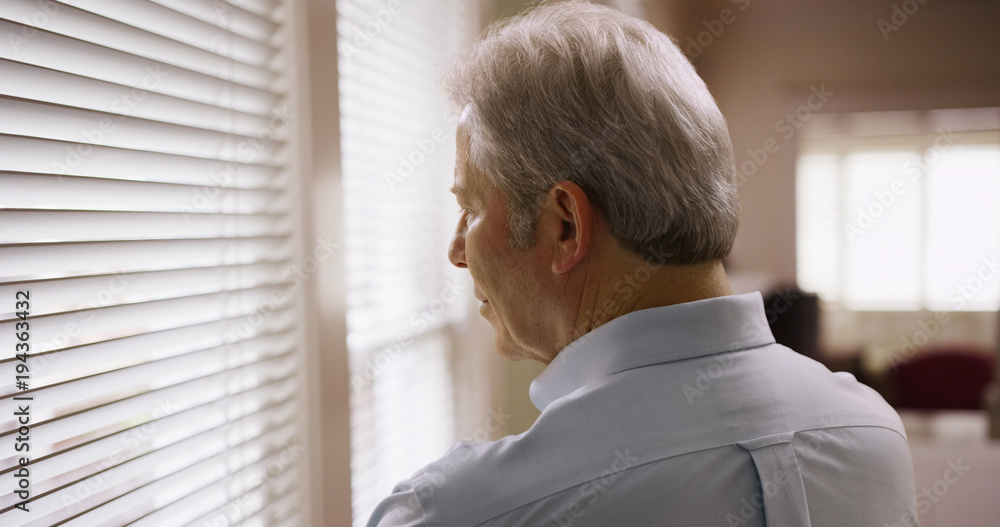 Closeup of mature caucasian man looking through window blinds Closeup of mature caucasian man looking through window blinds