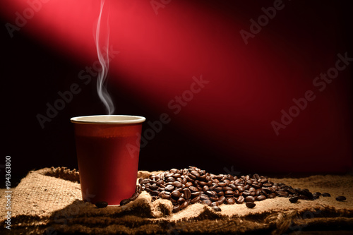Paper cup of coffee with smoke and coffee beans on reddish brown background
