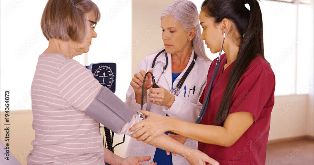 A patient gets her blood pressure taken by a doctor and a nurse. Two medical professionals take the blood pressure from their elderly patient