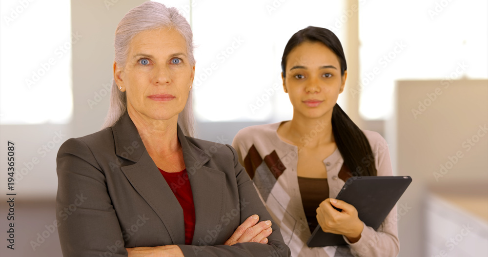 A business executive and her secretary pose for a portrait at work. Two women at work look at the camera A business executive and her secretary pose for a portrait at work. Two women at work look at the camera