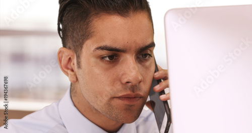 Hispanic Business man on cell phone and computer with. Latino businessman in office using cellphone. Young professional worker in his 20s