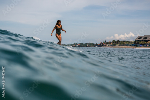 Canvas Print Beautiful young indonesian woman in bikini surfing wave in Bali on the backgroun