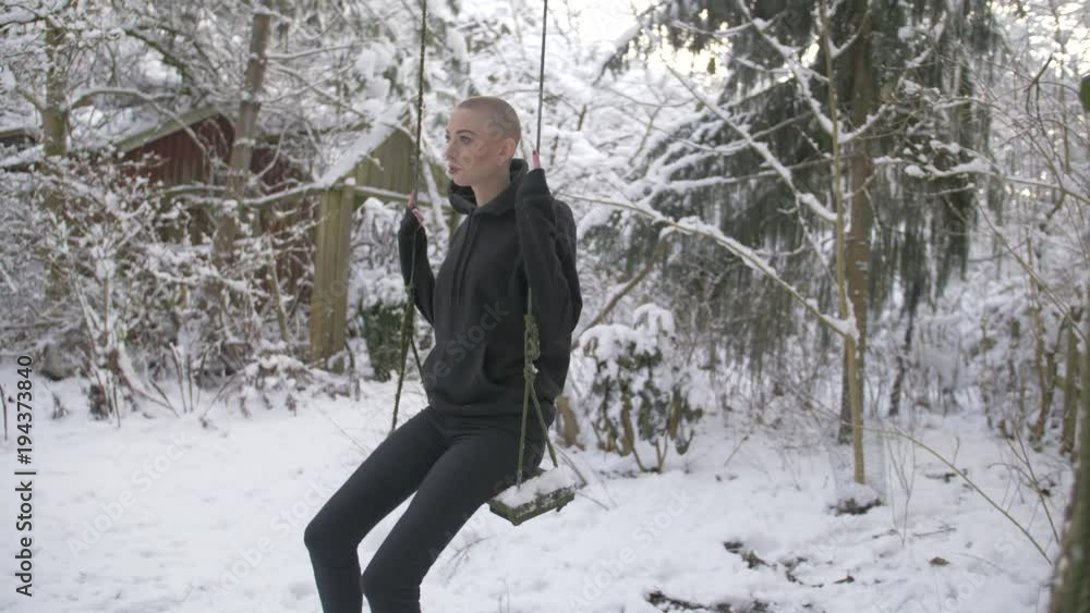 Young woman looks worried and sad, sitting on a swing during winter