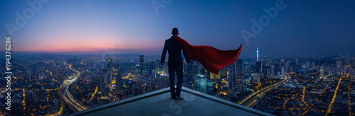 Businessman in suit and cape hero stand at rooftop looking great cityscape view and thinking business plan of the future . Night scene . photo