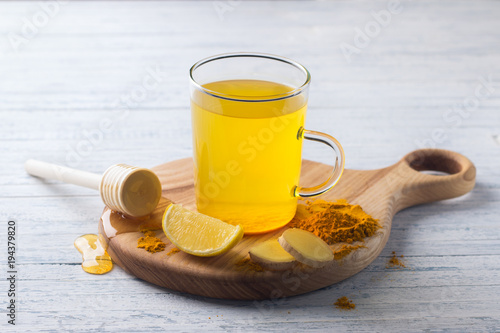 Energy tonic drink with turmeric, ginger, lemon and honey on a wooden board, selective focus