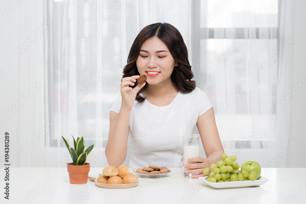 Pretty young asian woman eating tasty cookie at home.