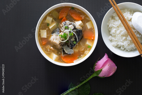 Japanese soup hot (Miso) with head salmon and rice in white bowl on brown wooden table, Decoration with pink rose