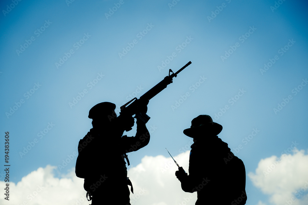 Silhouette image of two armed soldiers with blue sky background Silhouette image of two armed soldiers with blue sky background