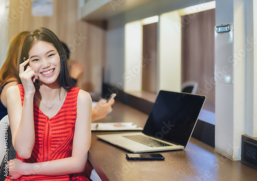 Beautiful Asian female businesswoman wearing a red dress with a laptop and smiling bright and confident in the work. © Fluky