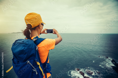  woman hiker taking photo with smartphone on seaside cliff