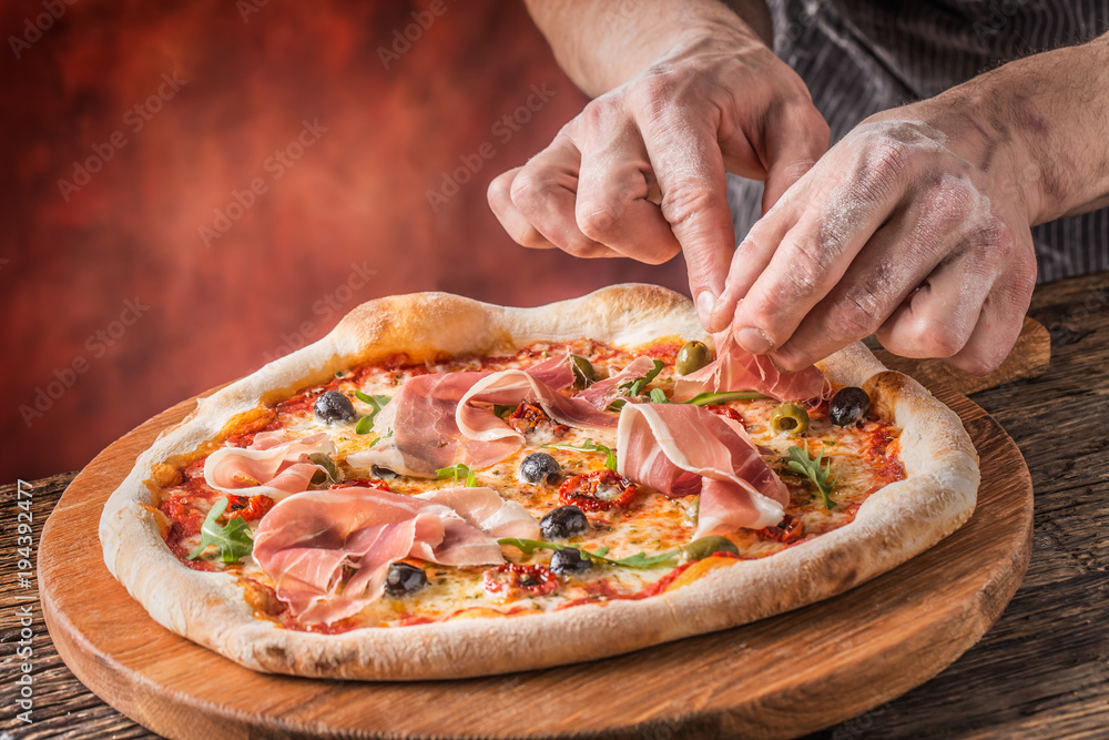 Pizza and Chef. Chef in the restaurant prepares a pizza and decorates it with  prosciutto