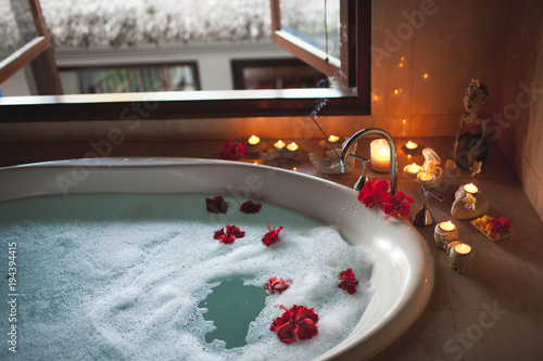 Large Filled Bath with Foam and Flowers. Romantic Atmosphere, Burning Scented Candles and Aromasticks