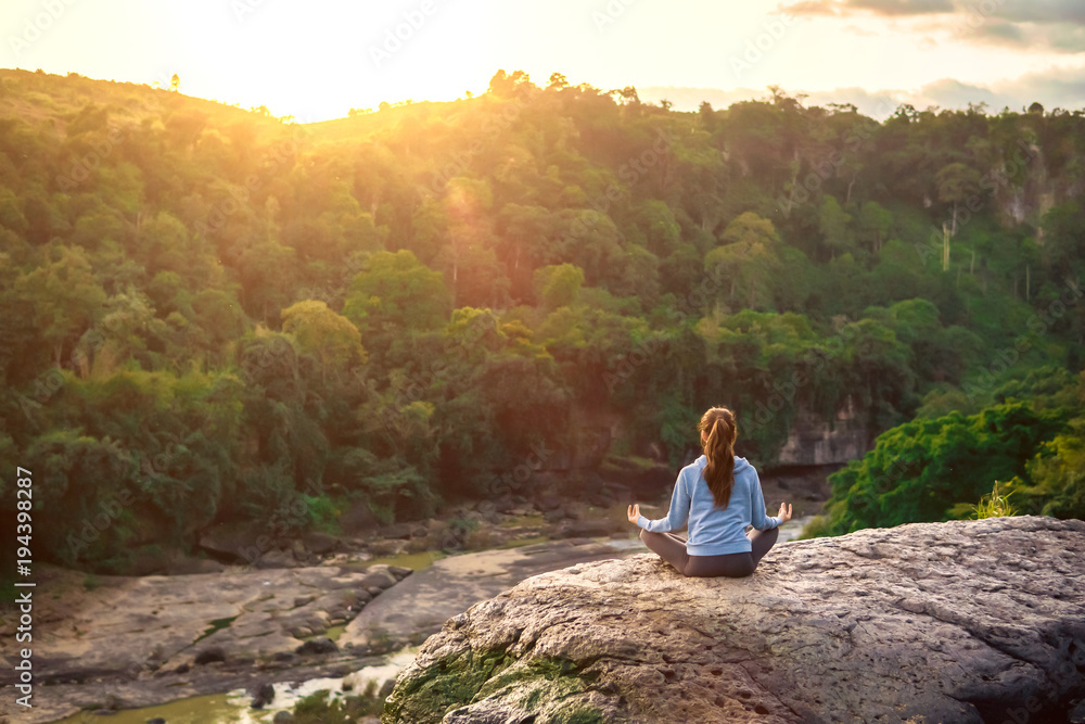 Yoga woman sit in lotus pose on mountain peak rock at sunrise