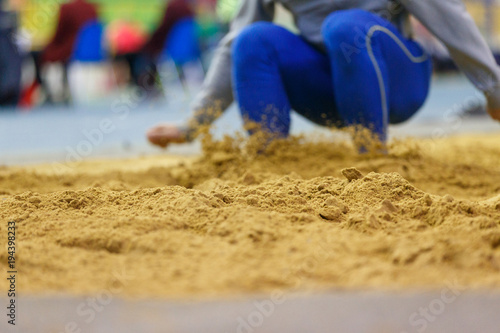 Sportsman landing into sandpit on training in long jump. Track and field competitions concept background