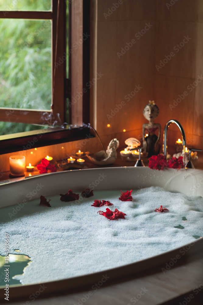 Large Filled Bath with Foam and Flowers. Romantic Atmosphere, Burning Scented Candles and Aromasticks