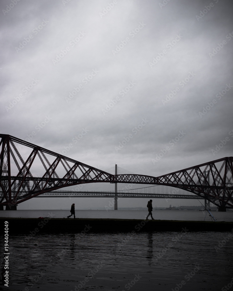 Two people walking along a pier infant of the Forth bridges