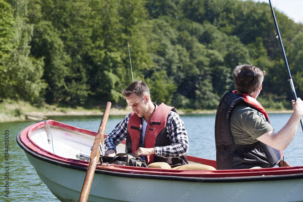 Son and father in boat make preparations for fish Son and father in boat make preparations for fish