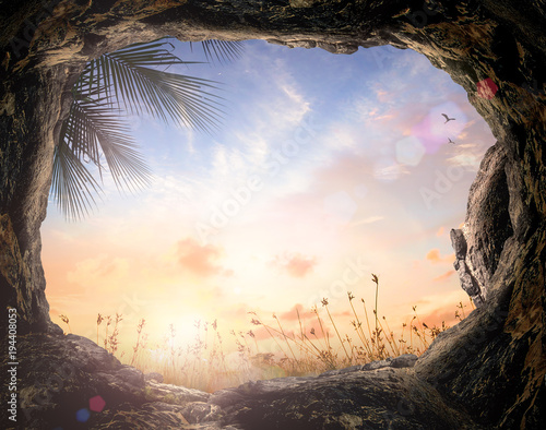 Easter Religious concept: Empty tomb stone with palm leaves over meadow sunset background