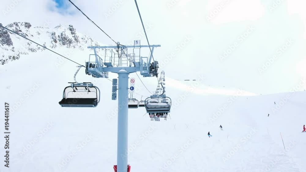 View from the open lift in motion upstairs, four-seat lifts work at the ski resort, downhill skiing and snowboarding tourists, slow motion. View from the open lift in motion upstairs, four-seat lifts work at the ski resort, downhill skiing and snowboarding tourists, slow motion.