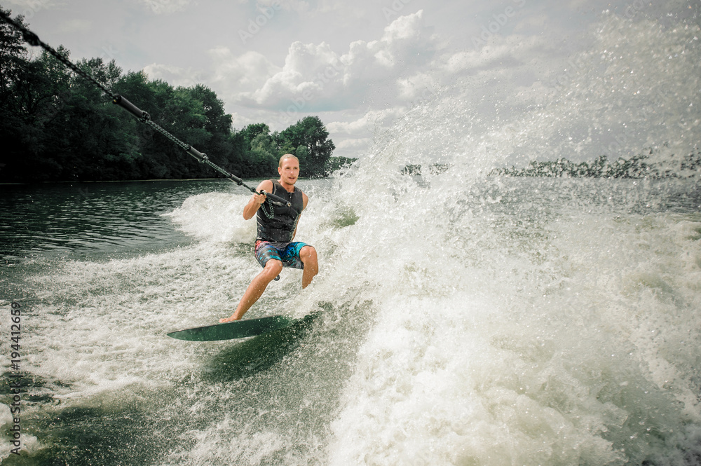 Young and athletic man wakesurfing on the board against the sky Young and athletic man wakesurfing on the board against the sky