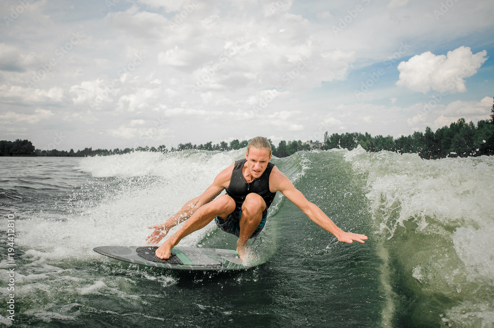 Fototapeta premium Young and athletic man wakesurfing on the board down the river