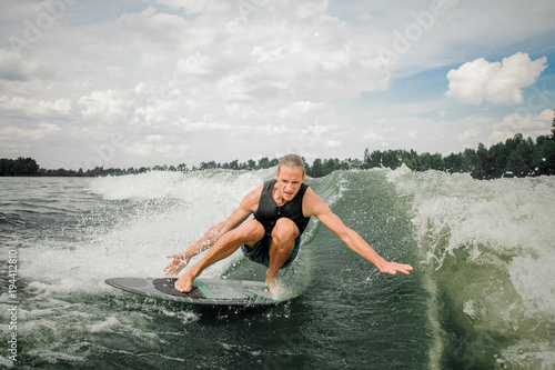 Young and athletic man wakesurfing on the board down the river