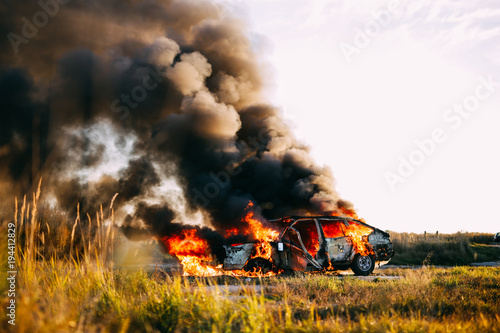 Car burning with open flames and black smoke on a field