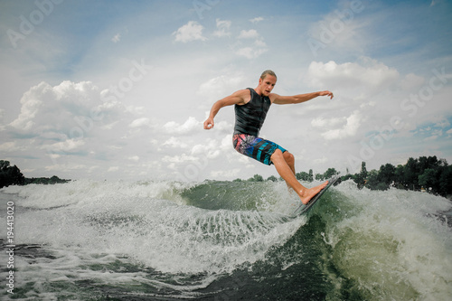 Handsome athletic guy wakesurfing on the board against the sky